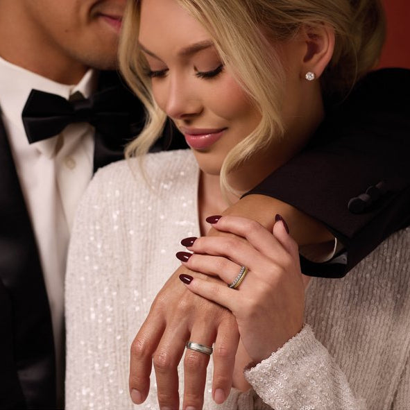 Couple in formal attire with a focus on hands wearing rings.